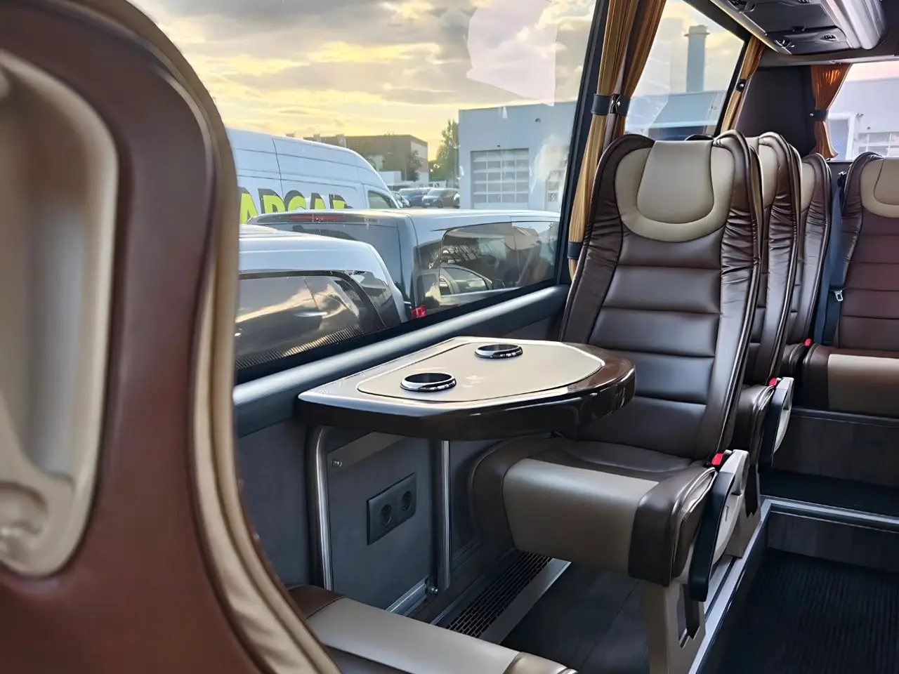 Innenraum eines Reisebusses mit braunen Ledersitzen und kleinem Tisch mit Getränkehaltern am Fenster.
