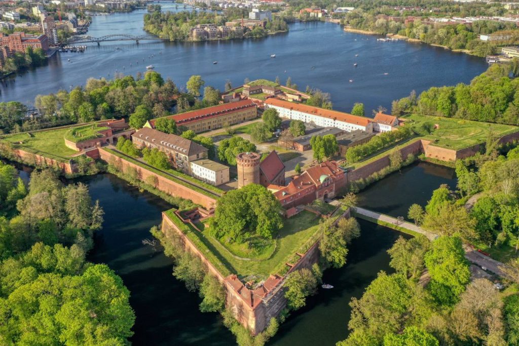 Luftaufnahme der Zitadelle Spandau in Berlin, umgeben von Wassergräben, Grünflächen und umliegender Stadtlandschaft.