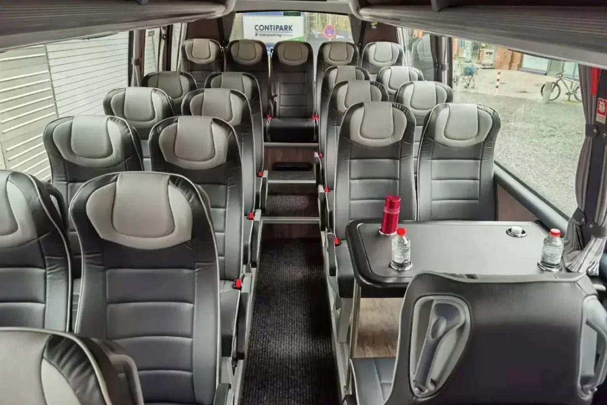 Innenraum eines Reisebusses mit grauen Ledersitzen und einem Tisch mit Wasserflaschen.
