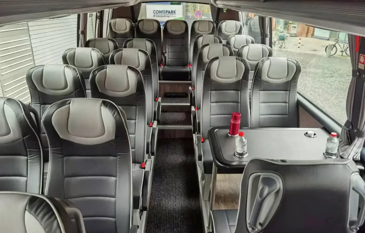 Innenraum eines Reisebusses mit grauen Ledersitzen und einem Tisch mit Wasserflaschen.