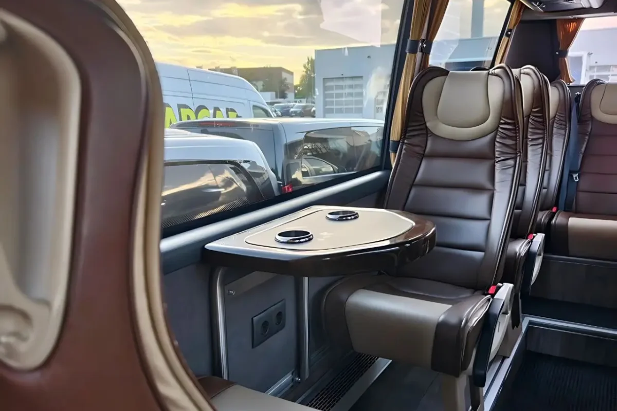 Innenraum eines Reisebusses mit braunen Ledersitzen und kleinem Tisch mit Getränkehaltern am Fenster.