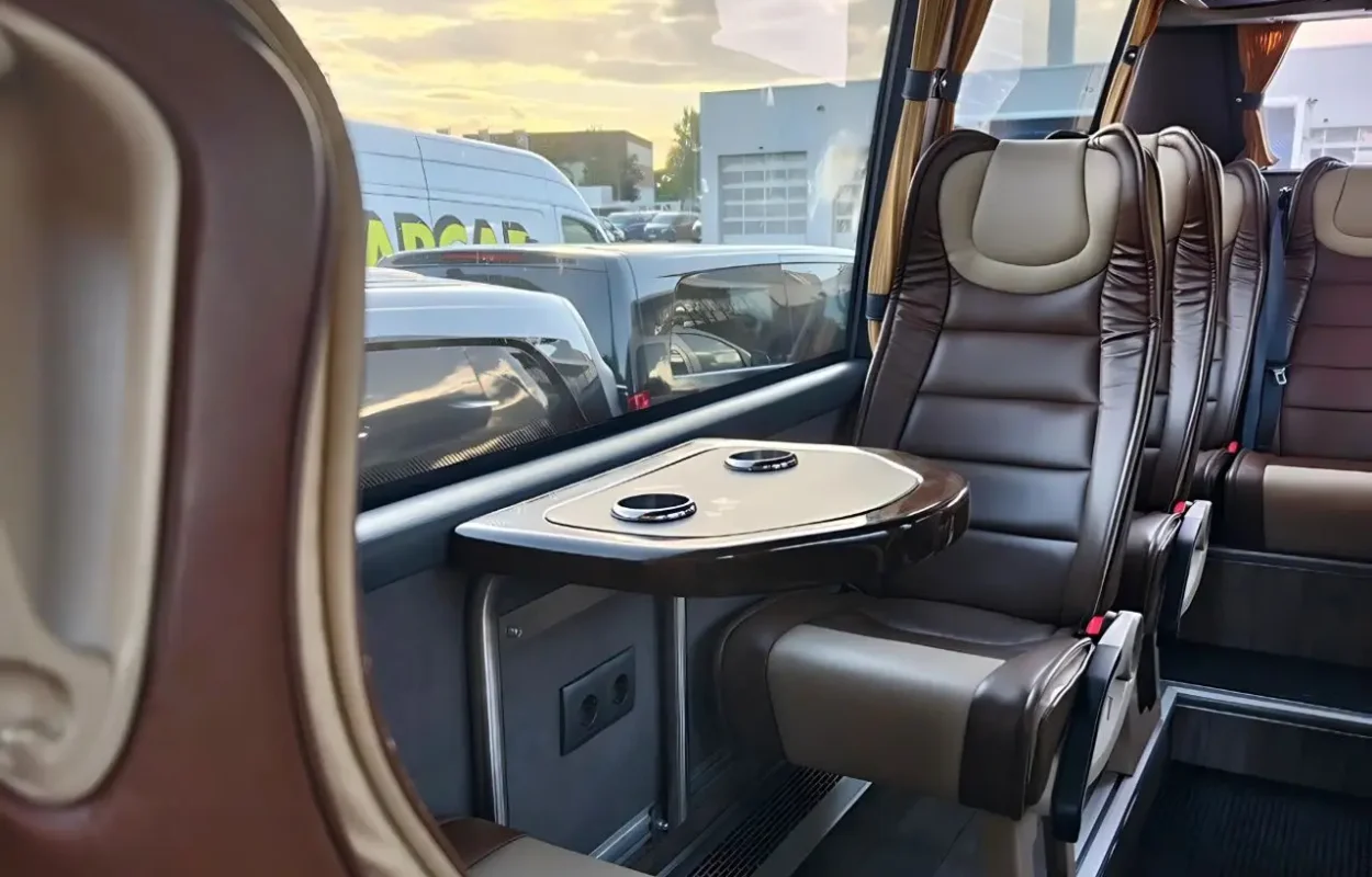 Innenraum eines Reisebusses mit braunen Ledersitzen und kleinem Tisch mit Getränkehaltern am Fenster.